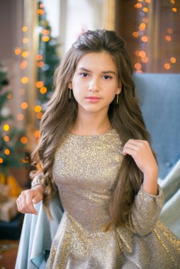 Noel 'de parlak çelenklerle süslenmiş parlak elbiseli, uzun kıvırcık saçlı tatlı bir genç kız. Noel havası. güzellik ve moda