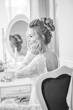 Sabah düğün saç stili ve makyajlı genç ve güzel bir gelin yatak odası masasının yanında, yere kadar uzanan beyaz dantelli bir ceketle. düğün sabahı