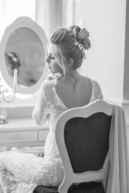 Sabah düğün saç stili ve makyajlı genç ve güzel bir gelin yatak odası masasının yanında, yere kadar uzanan beyaz dantelli bir ceketle. düğün sabahı