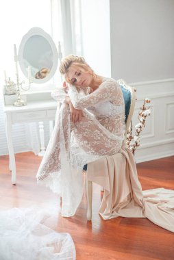 Sabah düğün saç stili ve makyajlı genç ve güzel bir gelin yatak odası masasının yanında, yere kadar uzanan beyaz dantelli bir ceketle. düğün sabahı