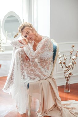 Sabah düğün saç stili ve makyajlı genç ve güzel bir gelin yatak odası masasının yanında, yere kadar uzanan beyaz dantelli bir ceketle. düğün sabahı