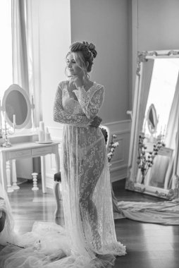 Sabah düğün saç stili ve makyajlı genç ve güzel bir gelin yatak odası masasının yanında, yere kadar uzanan beyaz dantelli bir ceketle. düğün sabahı