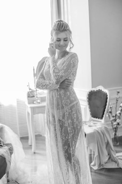 Sabah düğün saç stili ve makyajlı genç ve güzel bir gelin yatak odası masasının yanında, yere kadar uzanan beyaz dantelli bir ceketle. düğün sabahı