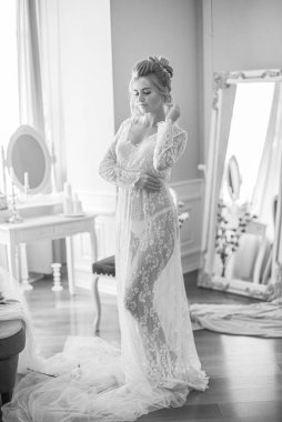 Sabah düğün saç stili ve makyajlı genç ve güzel bir gelin yatak odası masasının yanında, yere kadar uzanan beyaz dantelli bir ceketle. düğün sabahı
