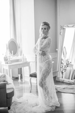 Sabah düğün saç stili ve makyajlı genç ve güzel bir gelin yatak odası masasının yanında, yere kadar uzanan beyaz dantelli bir ceketle. düğün sabahı