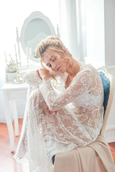 一位年轻貌美的新娘 早上在闺房桌旁穿着一条地板长的白色花边紧身衣 有着婚纱的发型和妆容 婚礼早上 — 图库照片