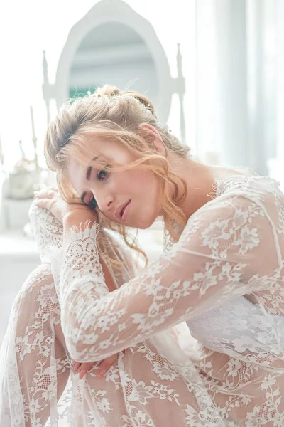 一位年轻貌美的新娘 早上在闺房桌旁穿着一条地板长的白色花边紧身衣 有着婚纱的发型和妆容 婚礼早上 — 图库照片