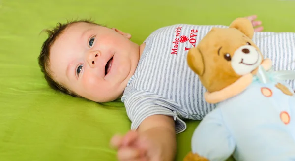 Sorrindo bebê jaz na cama com brinquedo — Fotografia de Stock