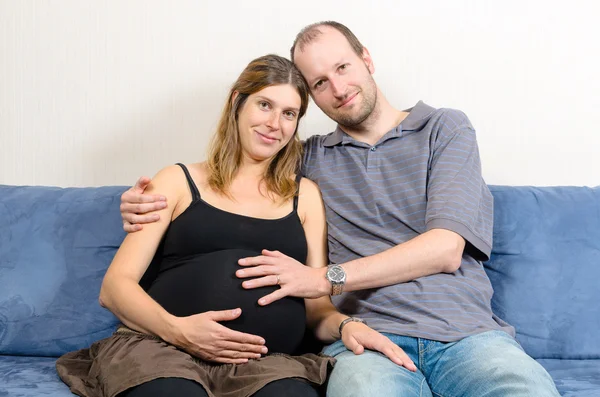 Счастливый муж обнимает беременную жену на диване — стоковое фото