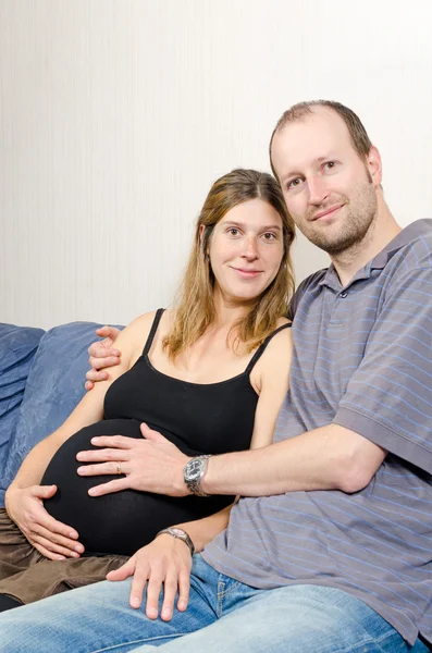 Glücklicher Ehemann umarmt seine schwangere Frau auf der Couch — Stockfoto
