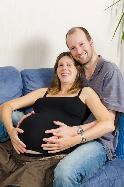 Happy husband embracing his pregnant wife on couch — Stock Photo, Image