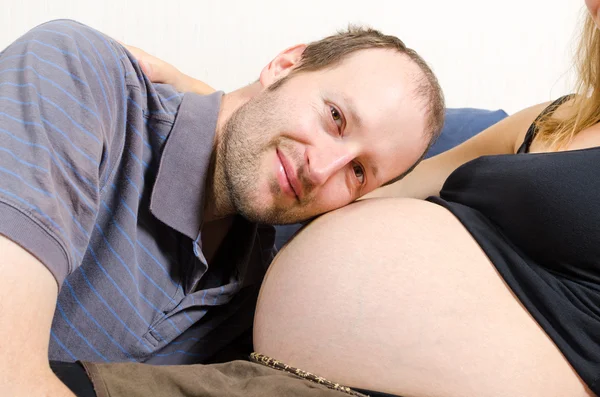 Marido feliz deitado na barriga de sua esposa grávida no sofá — Fotografia de Stock