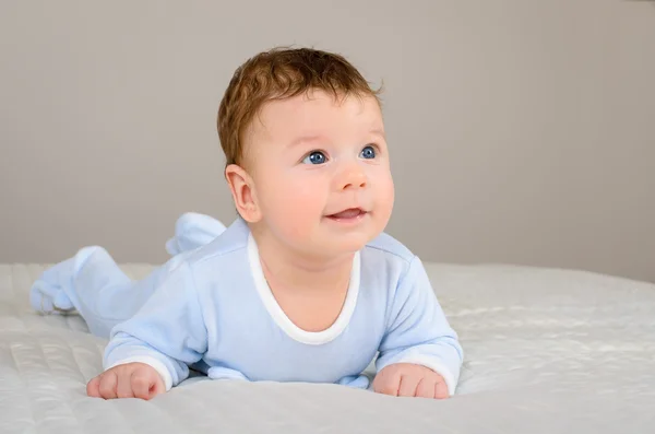 Cute smiling baby boy in bed lying on his belly in bedroom — Stock Photo, Image
