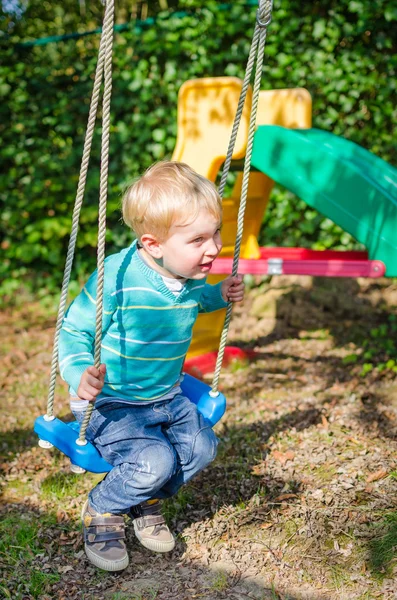 Lindo niño rubio balanceándose en columpios patio al aire libre — Foto de Stock