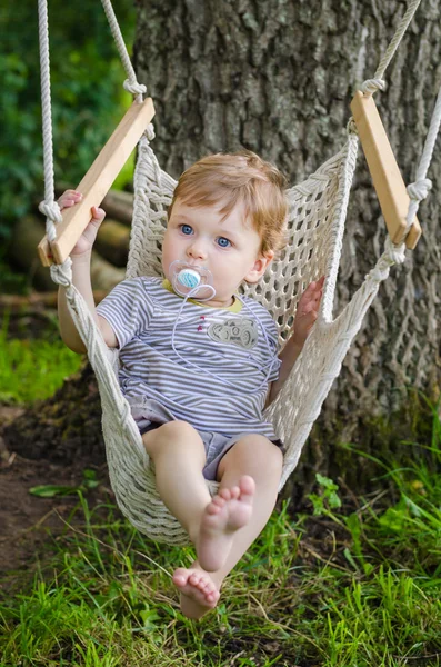 Pequeño niño lindo que monta en oscilación de la hamaca en el parque —  Fotos de Stock