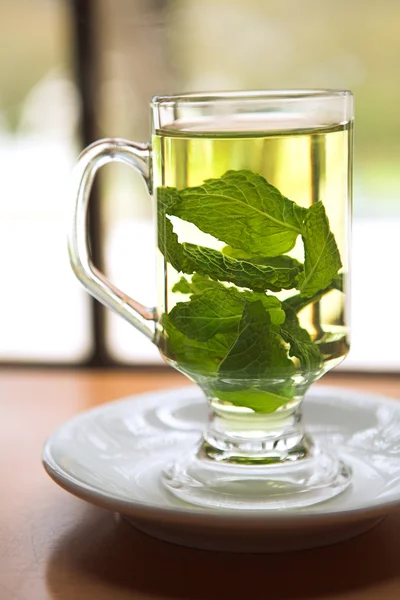 Hot green mint tea standing next to a window with whole mint leaves — Stock Photo, Image