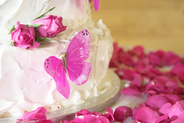 Vanille-Hochzeitstorte mit weißem Zuckerguss, Rosenblättern und rosa Schmetterlingen — Stockfoto