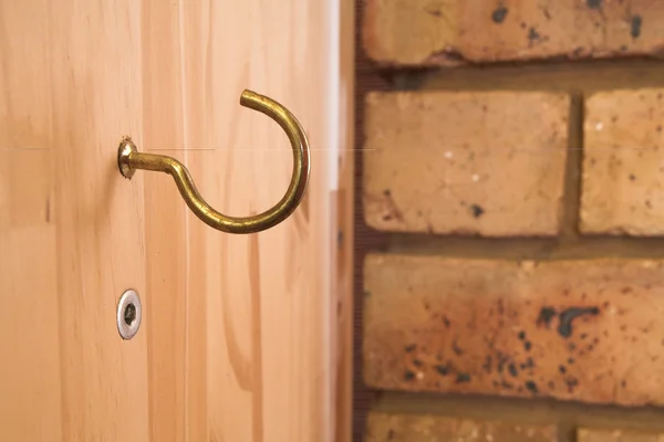 Hook on wooden panel, brick wall in background — Stock Photo, Image