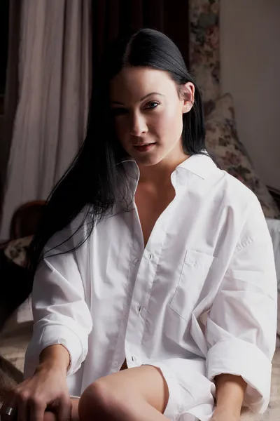 Young adult Caucasian wearing only a white shirt, sitting on a bed — Stock Photo, Image