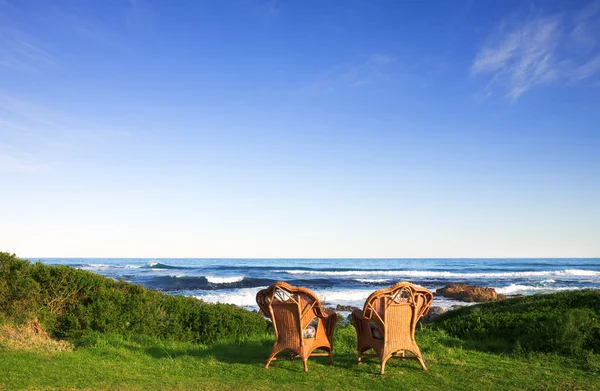 Wicker cane chairs on a lawn next to the sea — Stock Photo, Image