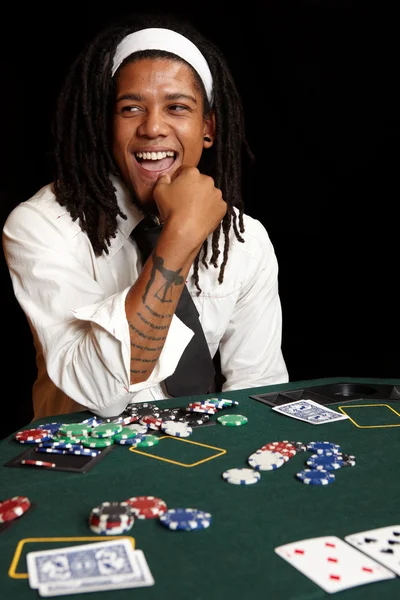 Africký mladík s dredy hrací karty, žetony a hráči her kolem zelené cítil pokerový stůl — Stock fotografie