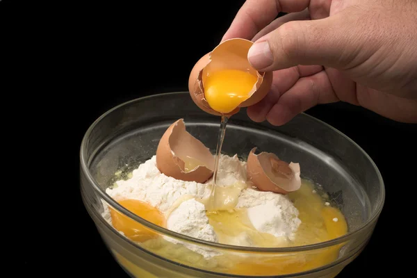 Hand breaking an egg into a glass bowl with flour — Stock Photo, Image