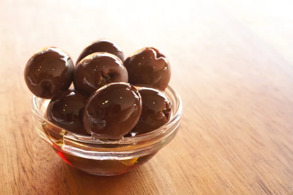 Small glass bowl of pitted black kalamata olives in oil on a brown wooden table — Stock Photo, Image