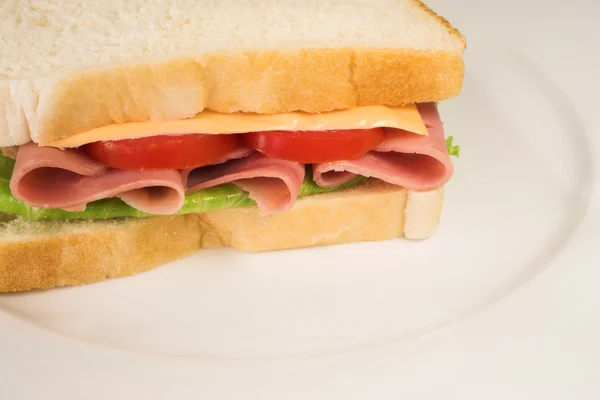 Sanduíche de presunto, queijo, tomate e alface num prato branco — Fotografia de Stock