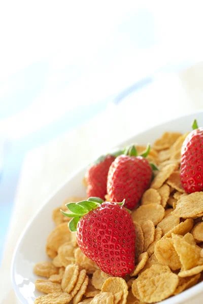 Färska röda jordgubbar och frukostflingor i en vit skål på ett köksbord — Stockfoto