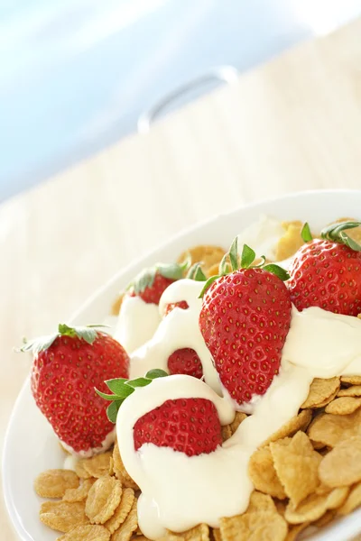 Fresh red strawberries and thick dairy cream on breakfast cereal in a white bowl on a kitchen table — Stock Photo, Image