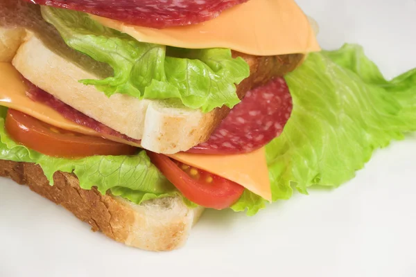 Sanduíche de salame, queijo, tomate e alface em um prato branco . — Fotografia de Stock