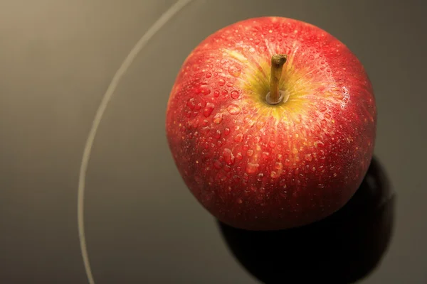 Manzana roja fresca con gotas de agua sobre un fondo de cristal negro — Foto de Stock