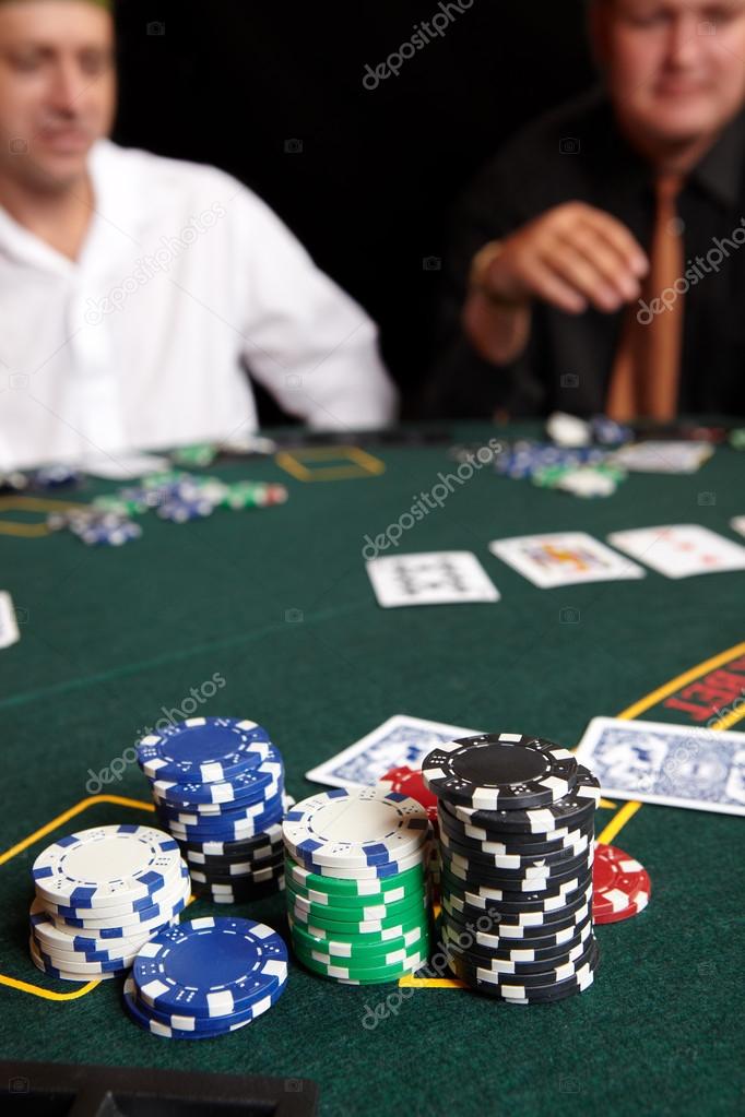 playing cards, chips and players gambling around a green felt poker table