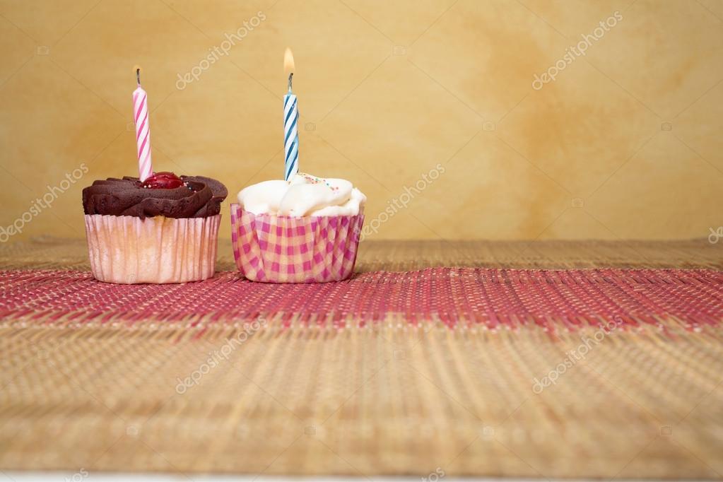 Two cupcakes on pink and brown table cloth in front of wall - copy space