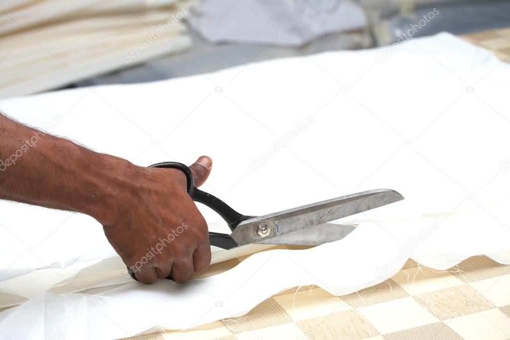 Man cutting white material with industrial sewing scissors, on a cutting table