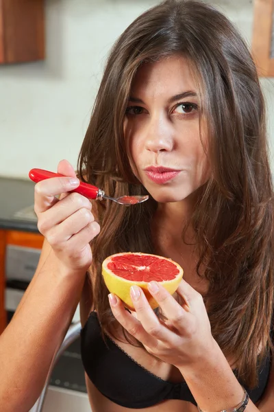 Sexy jonge volwassen brunette vrouw in zwarte lingerie eten een grapefruit — Stockfoto