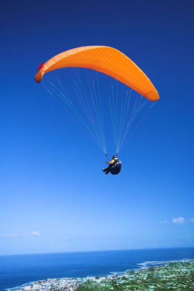 Paraglider launching from the ridge with an orange canopy and the sun from behind — Stock Photo, Image