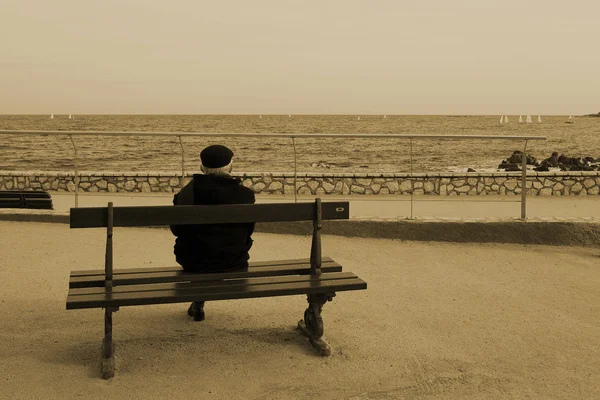 Человек на скамейке рядом с морем — стоковое фото