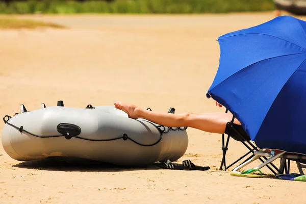 Mann entspannt sich am Strand unter blauem Sonnenschirm mit Boot — Stockfoto