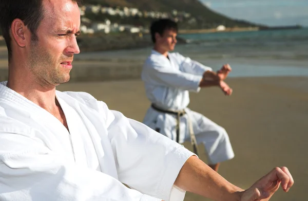 Young adult men with black belt practicing on the beach — Stock Photo, Image