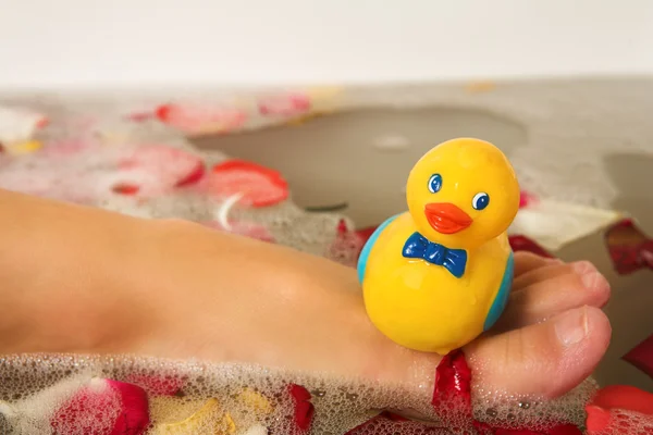 Plastic toy duck on the leg of a woman in a bath — Stock Photo, Image