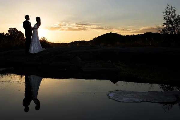 Bride and groom next to river at sunset — Stock Photo, Image