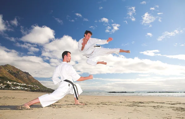 Young adult men with black belt practicing on the beach — Stock Photo, Image