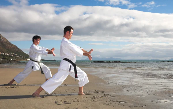 Young adult men with black belt practicing on the beach — Stock Photo, Image