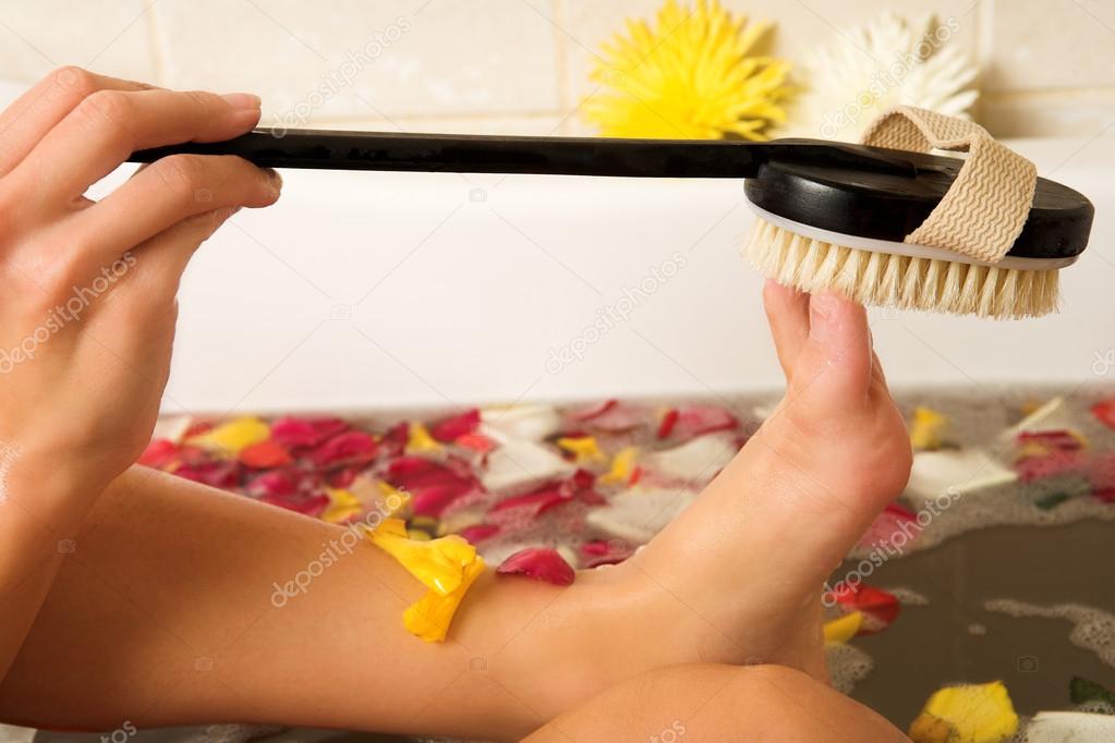 Woman in a bath scrubbing her feet with a brush