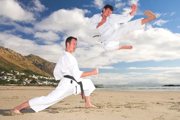 Young adult men with black belt practicing on the beach on a sunny day. — Stock Photo, Image