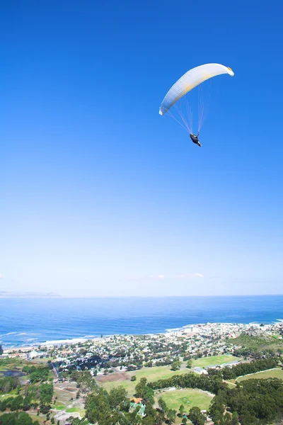 Parapente lançando do cume com um dossel laranja e branco e o sol por trás — Fotografia de Stock