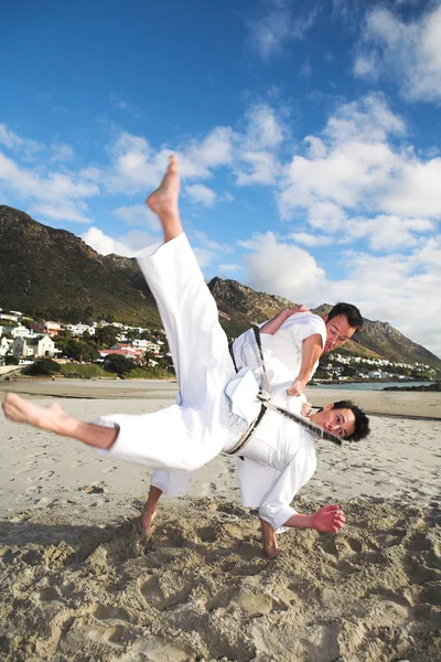 Young adult men with black belt practicing fighting on the beach on a sunny day — Stock Photo, Image