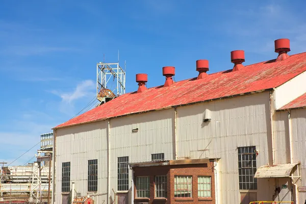 Corrugated iron building with red roof on mine premises with shaft winch in the background — Stock Photo, Image