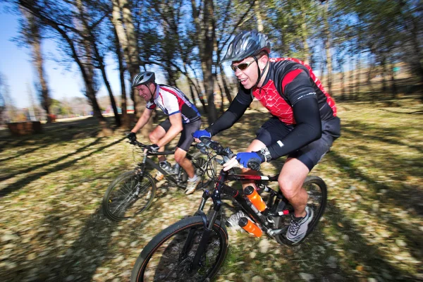 Panorámica de dos ciclistas de montaña, corriendo en un bosque . — Foto de Stock